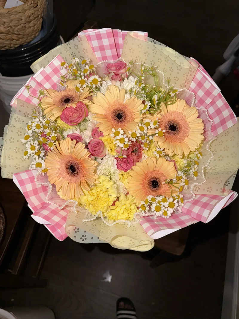 Peach gerbera daisies, chamomile and pink roses in a gingham and floral wrap.