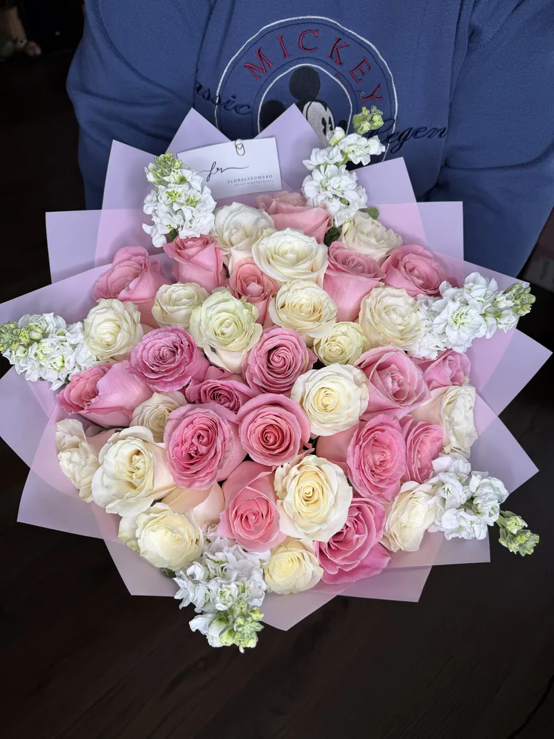 Pink, cream and white roses with white stock, wrapped in pale lilac paper.