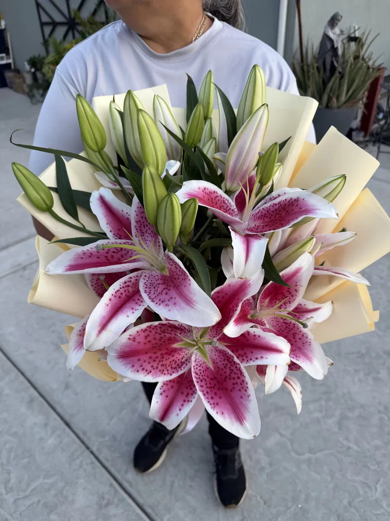 Pink stargazer lilies and unopened buds in a cream paper wrap.
