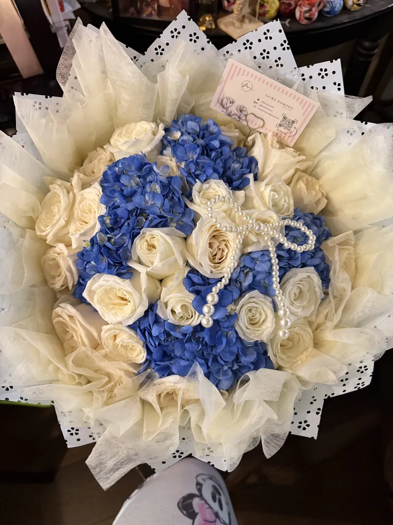 Cream roses and blue hydrangea gathered in ivory tulle with a pearl rosary laid across the blooms.
